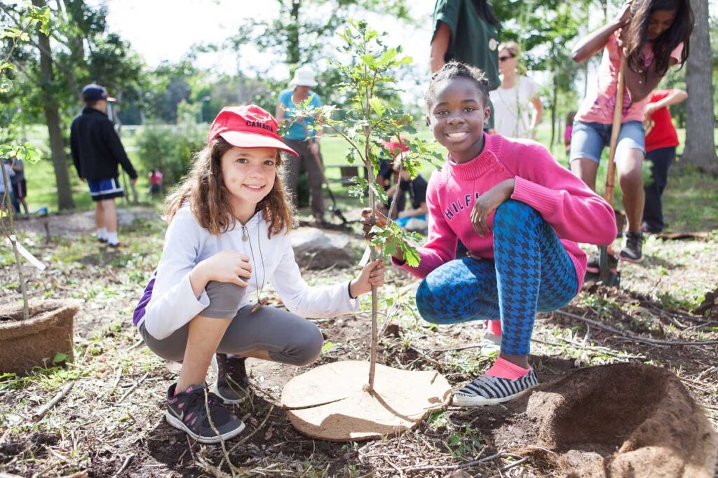 Two young girls holding a newly planted tree.