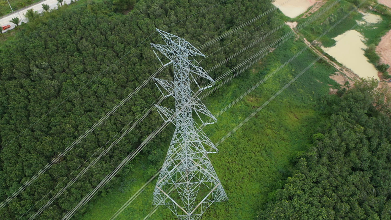 View from above of a hydro tower surrounded by forests on either side with a road to the left.